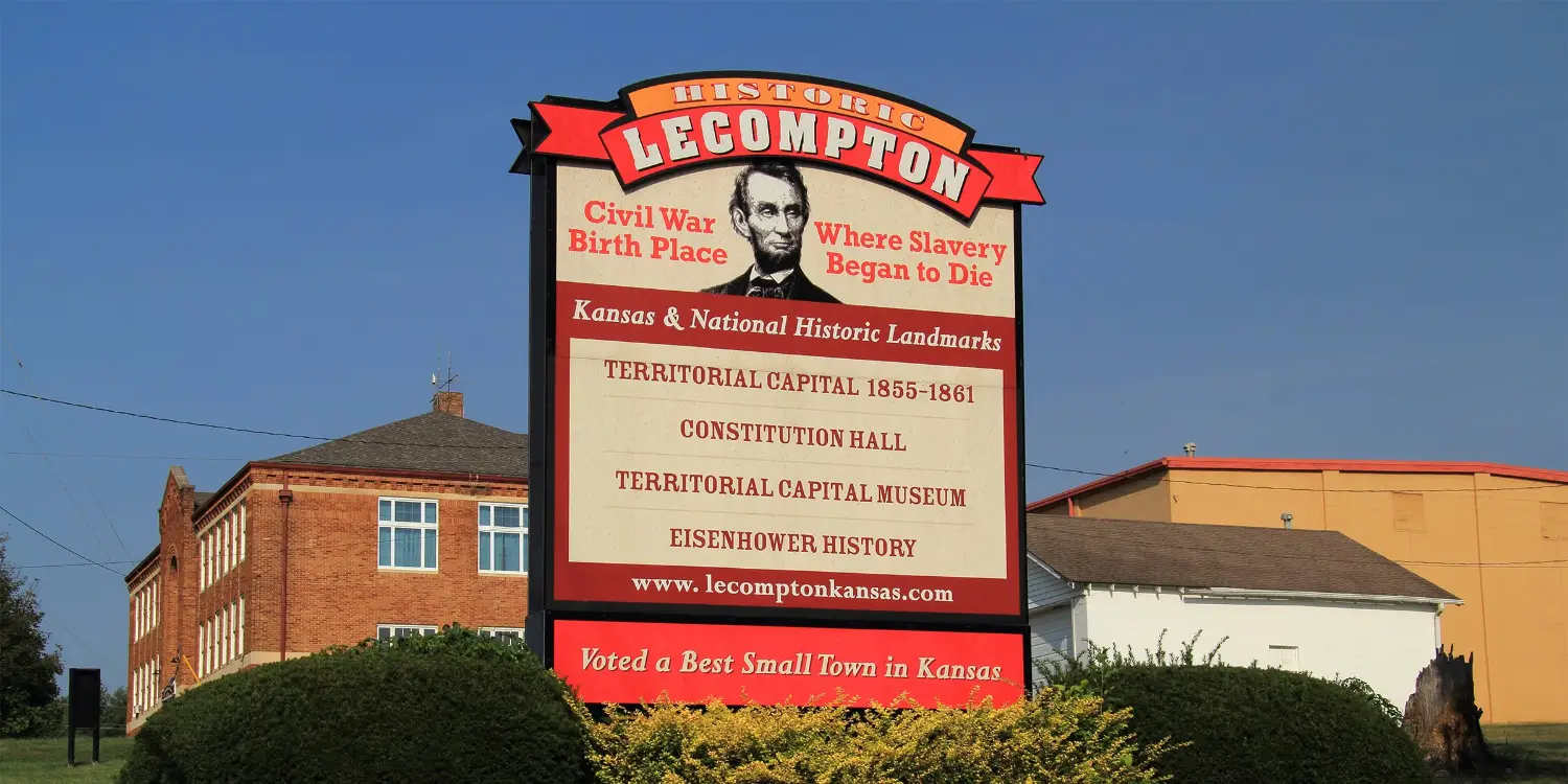 Historic Lecompton, Kansas sign lists Civil War, slavery, territorial capital, Constitution Hall, and museum landmarks beside brick buildings.