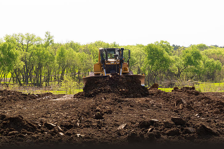 A bulldozer working on a dirt mound in a cleared area surrounded by greenery.
