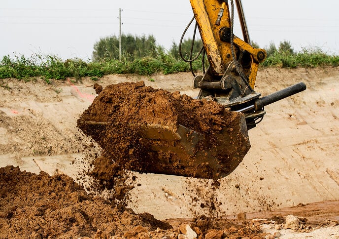 A close-up of an excavator's bucket lifting and dropping soil at a construction site.
