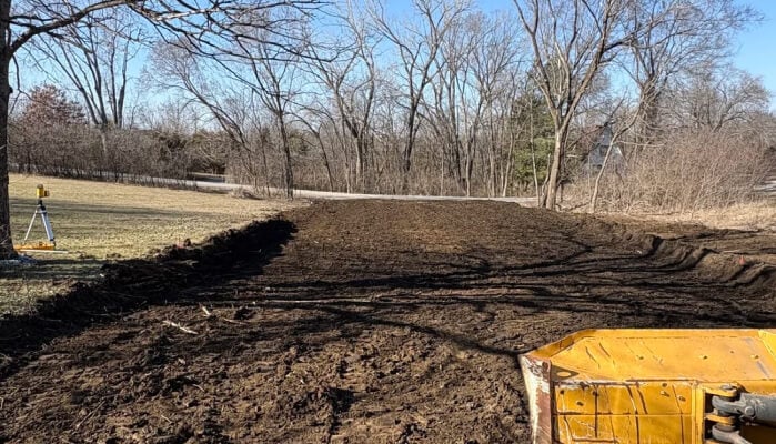 A cleared patch of soil in a field with trees in the background, and a construction vehicle in the foreground.