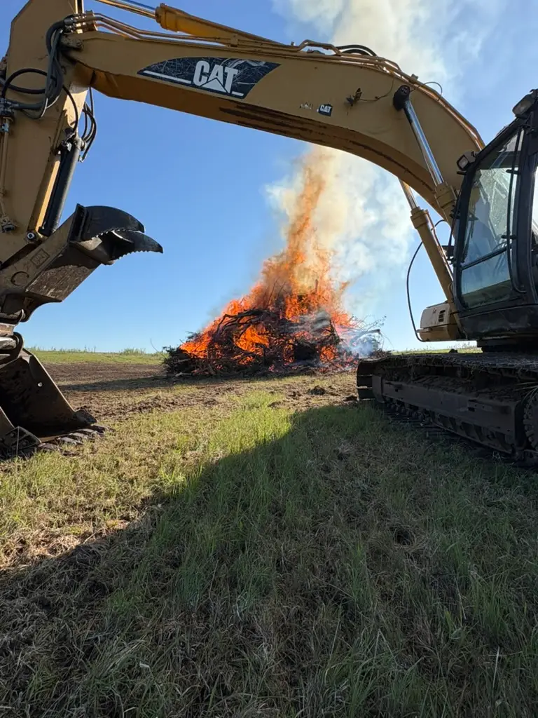 A yellow excavator and a burning branches in the back